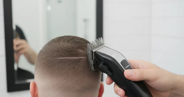 A close-up of the back of a man’s head as an electric clipper with a guard is used to blend the fade, smoothing the transition between different hair lengths.

