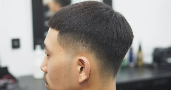 Asian man with a buzz cut fade haircut featuring a short textured top and a smooth mid fade on the sides and back.