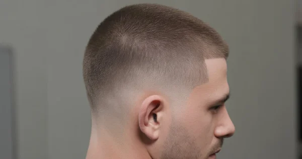 Man with a buzz cut con taper fade haircut featuring a short even buzz on top and a clean tapered fade around the sides and neckline.
