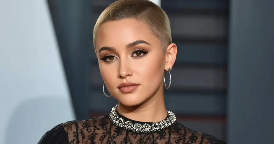 Close-up portrait of a Ariana Grande with a buzz cut hairstyle, wearing hoop earrings and a black lace outfit, looking directly at the camera with soft makeup and a neutral expression