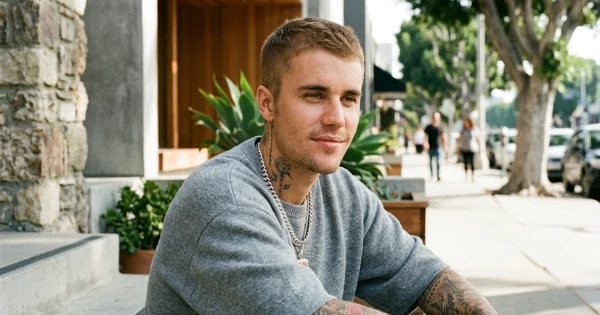 Justin Bieber showcasing a classic blonde buzz cut hairstyle while sitting outdoors in a grey sweatshirt.